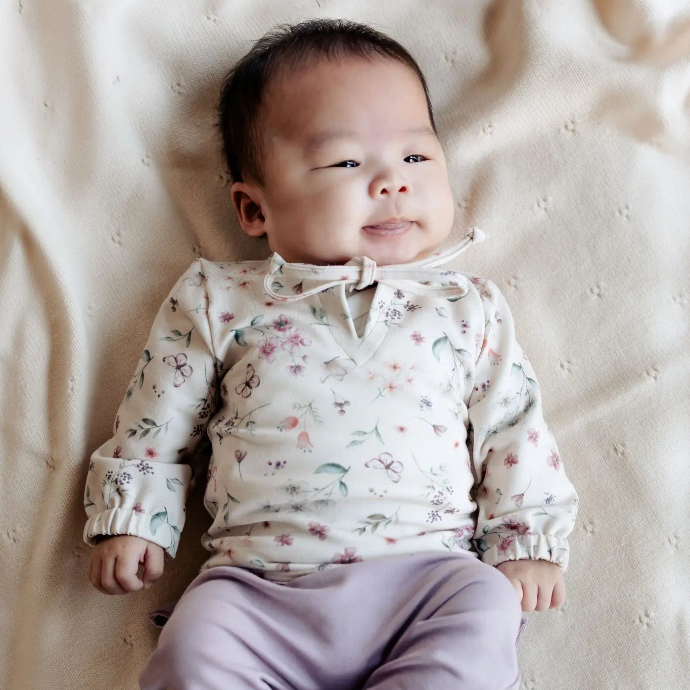 baby in Moalie setje bestaanden uit een lila broekje en gebloemde sweater