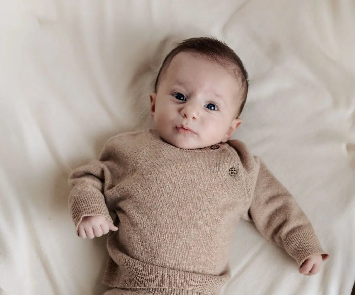 Baby in beige truitje, broekje en slofejs van merinowol en cashmere