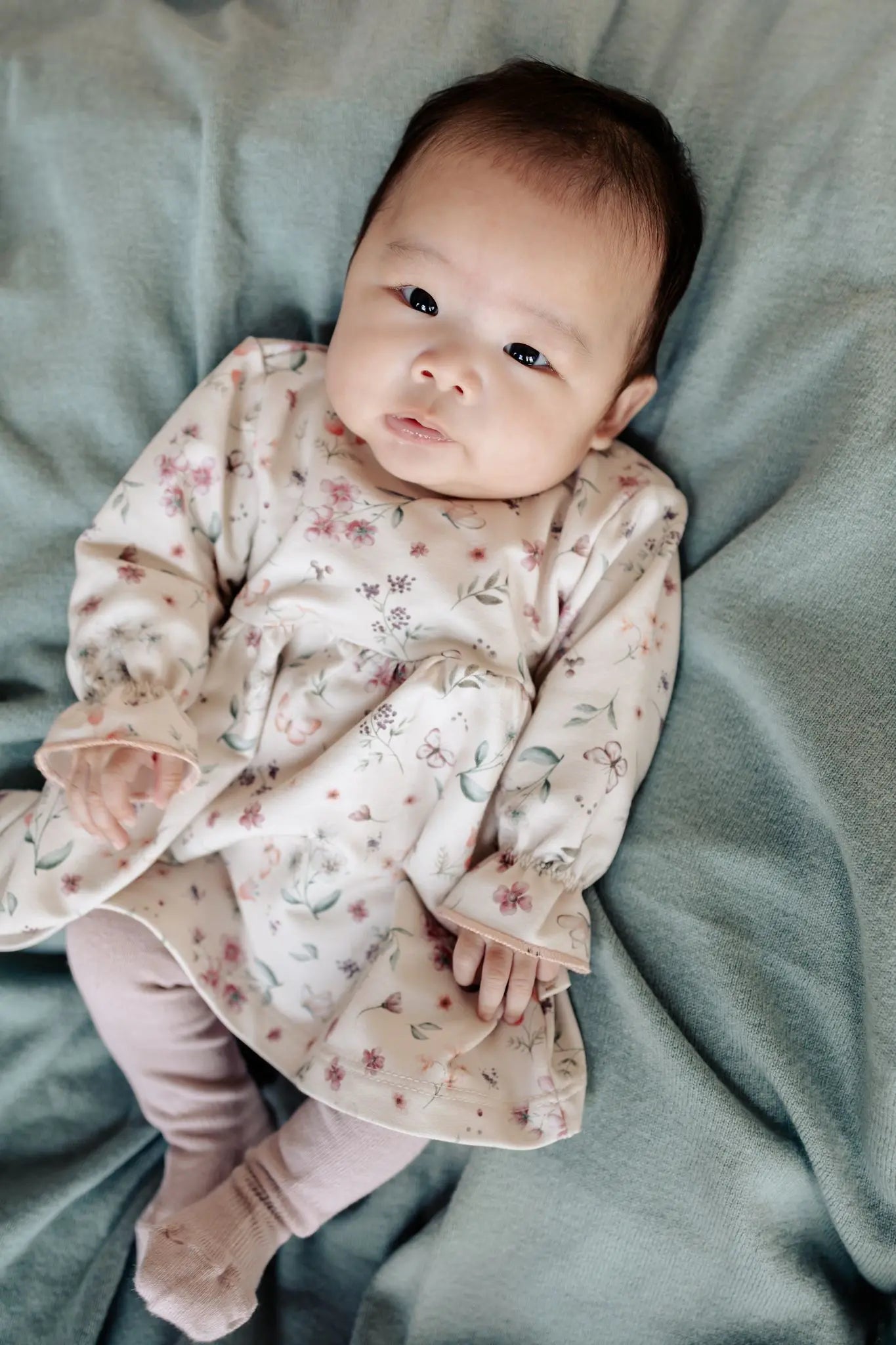 baby op een wollen sage groene deken die een Moalie jukrje draagt in zacht orze met bloemen en vlinder print