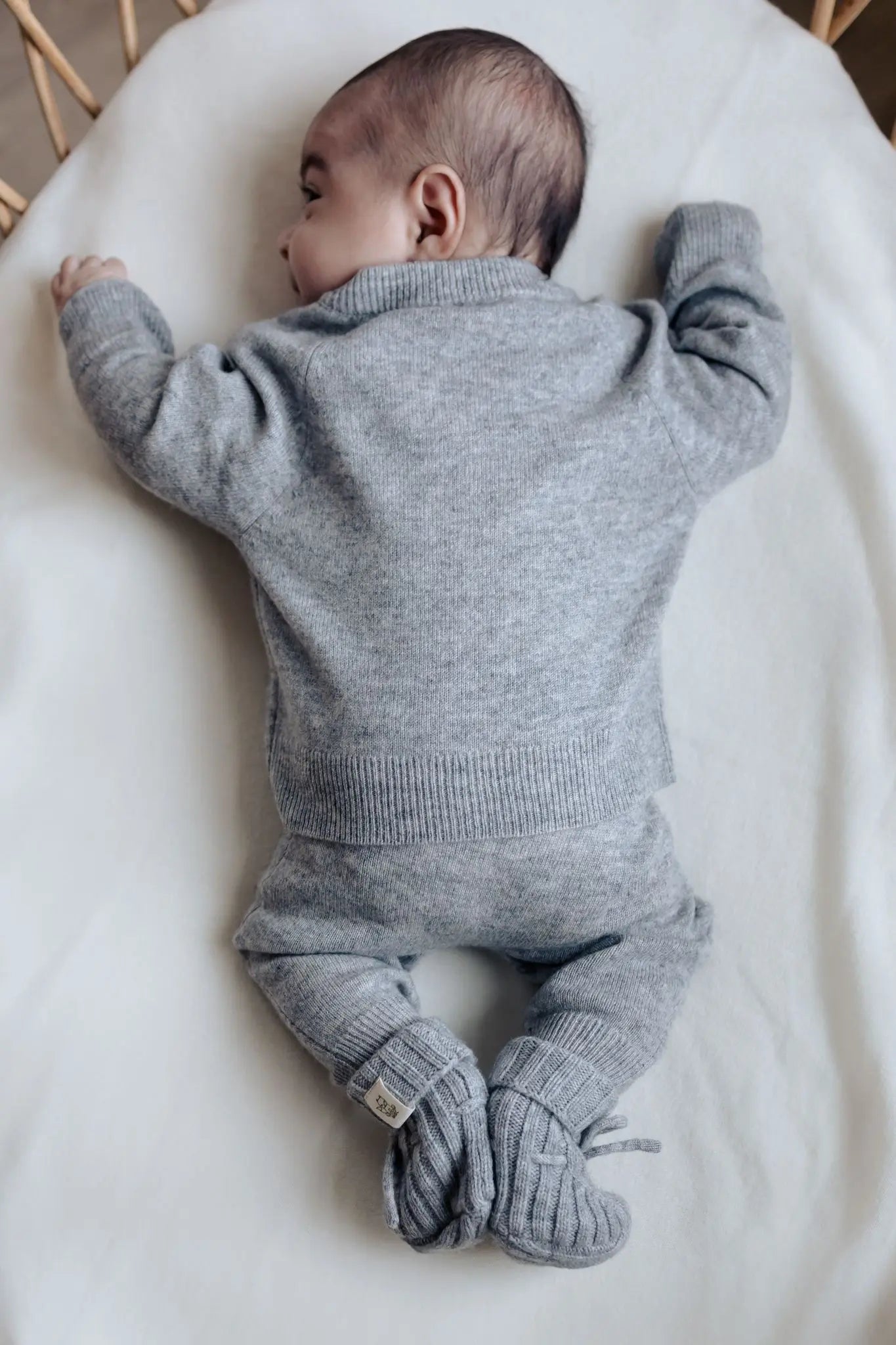 Baby in grijs wollen outfit in buikligging waardoor de achterkant van het wollen truitje en broekje goed te zien zijn. 