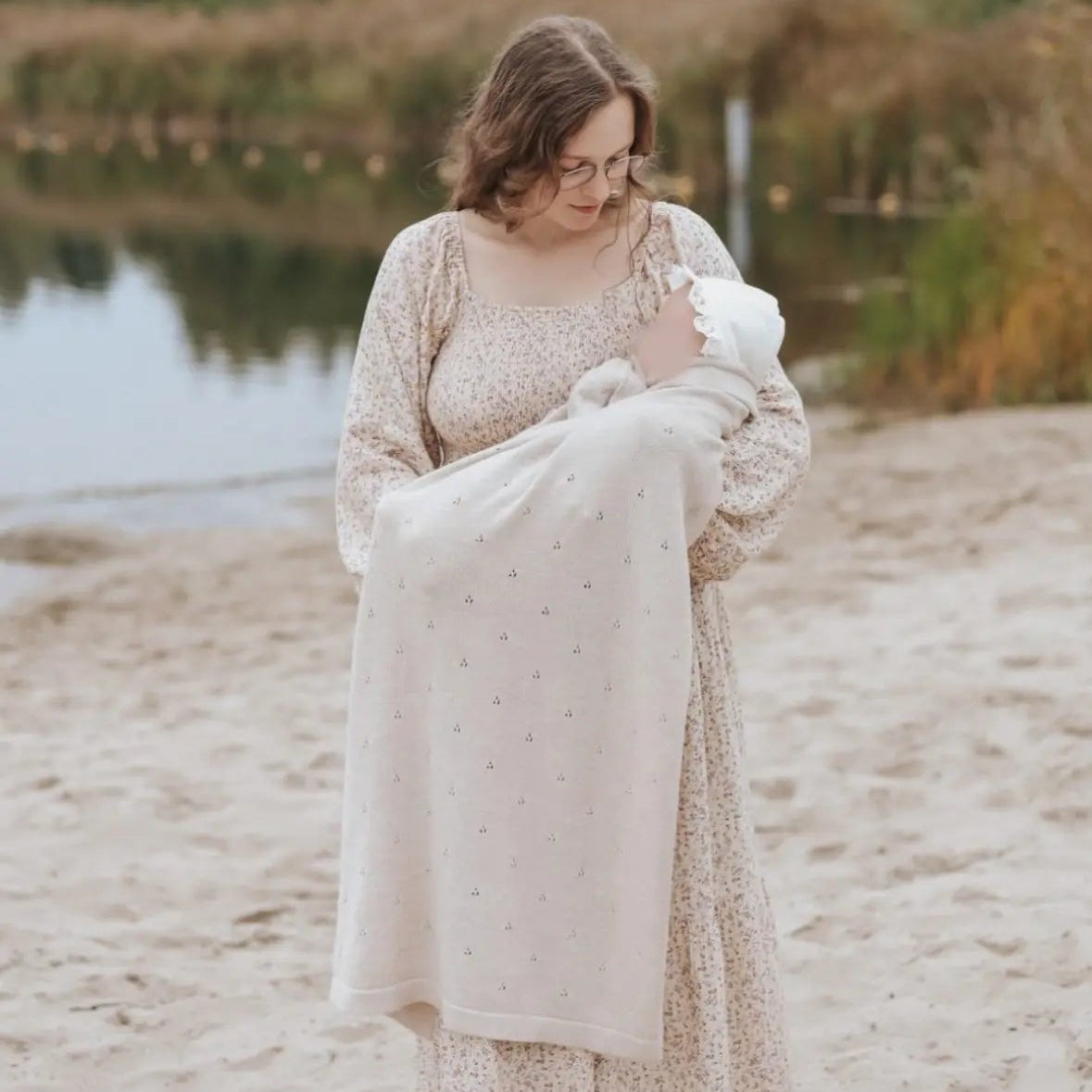 mama met baby op het strand. De baby is gewikkeld inde pointelle deken van Moalie. Gemakt ban beige, wasbare merinowol.