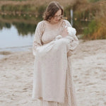 mama met baby op het strand. De baby is gewikkeld inde pointelle deken van Moalie. Gemakt ban beige, wasbare merinowol.