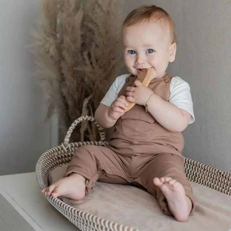 baby zittend in rieten mandje. De baby draagt een bruine tuinbroek van French terry 
