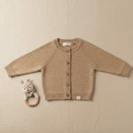 Baby vestje van merinowol en cashmere in warm beige op een linnen achtergrond naast het vestje de handgemaakte Moalie rammelaar van een gehaakte vos 