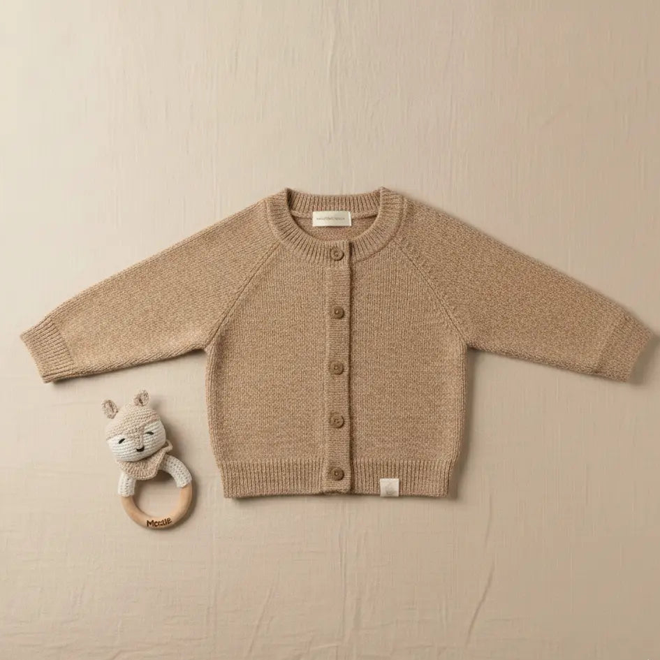 Baby vestje van merinowol en cashmere in warm beige op een linnen achtergrond naast het vestje de handgemaakte Moalie rammelaar van een gehaakte vos 