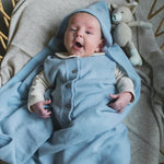 Gapende vrolijke baby in rotan wieg. Gewikkeld in een zacht blauwe deken van merinowol en cashmere. 