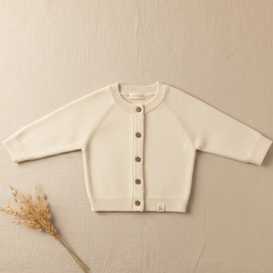 Foto van abyvestje merinowol en cashmere in creme kleur op een linnen  achtergond. op de foto ook een takje van droogbloemen.