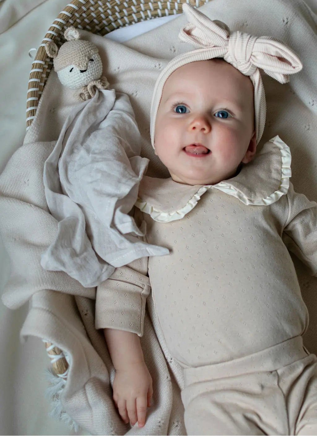 baby in rieten mandje. De baby draagt een  katoenen romper in beige pointelle. 