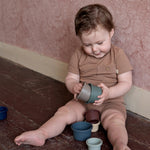 baby spelend op de grond, gekleed in een bruine katoenen outfit. 