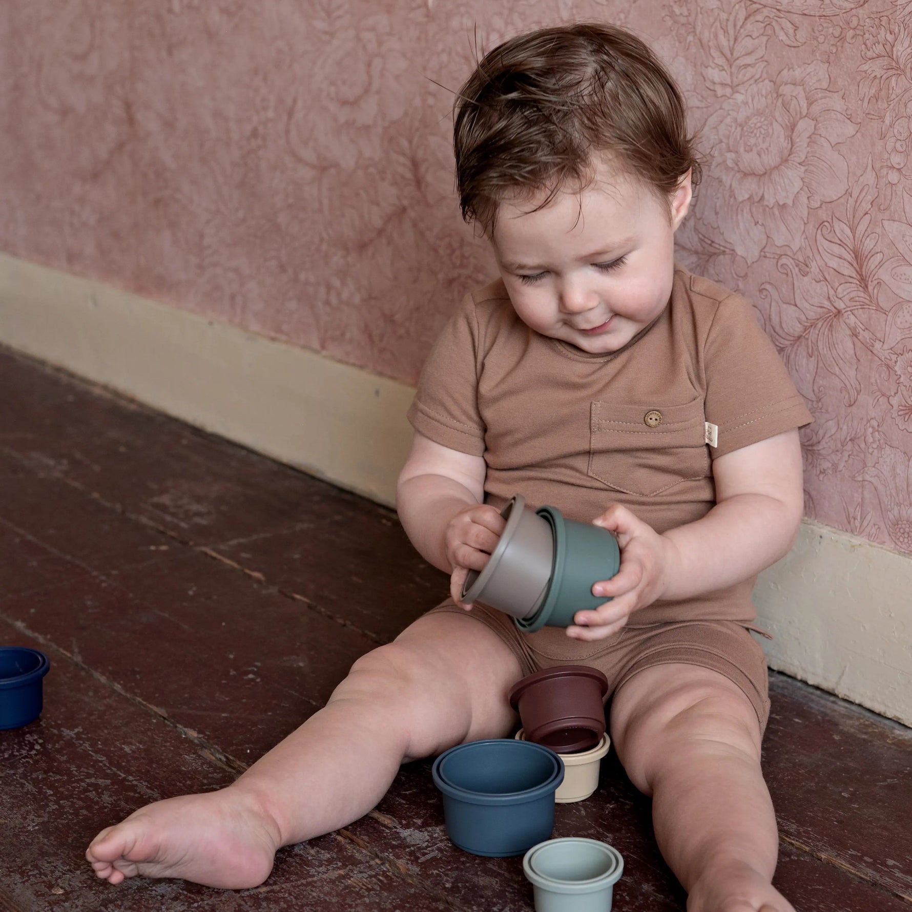 baby spelend op de grond, gekleed in een bruine katoenen outfit. 