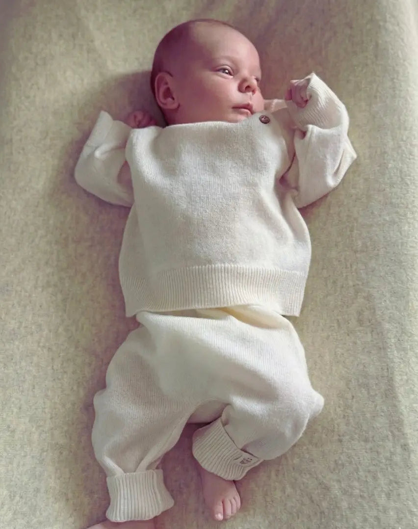 baby liggend op aan kleedkussen, gekleed in creme kleurig pakje van merinowol en cashmere 