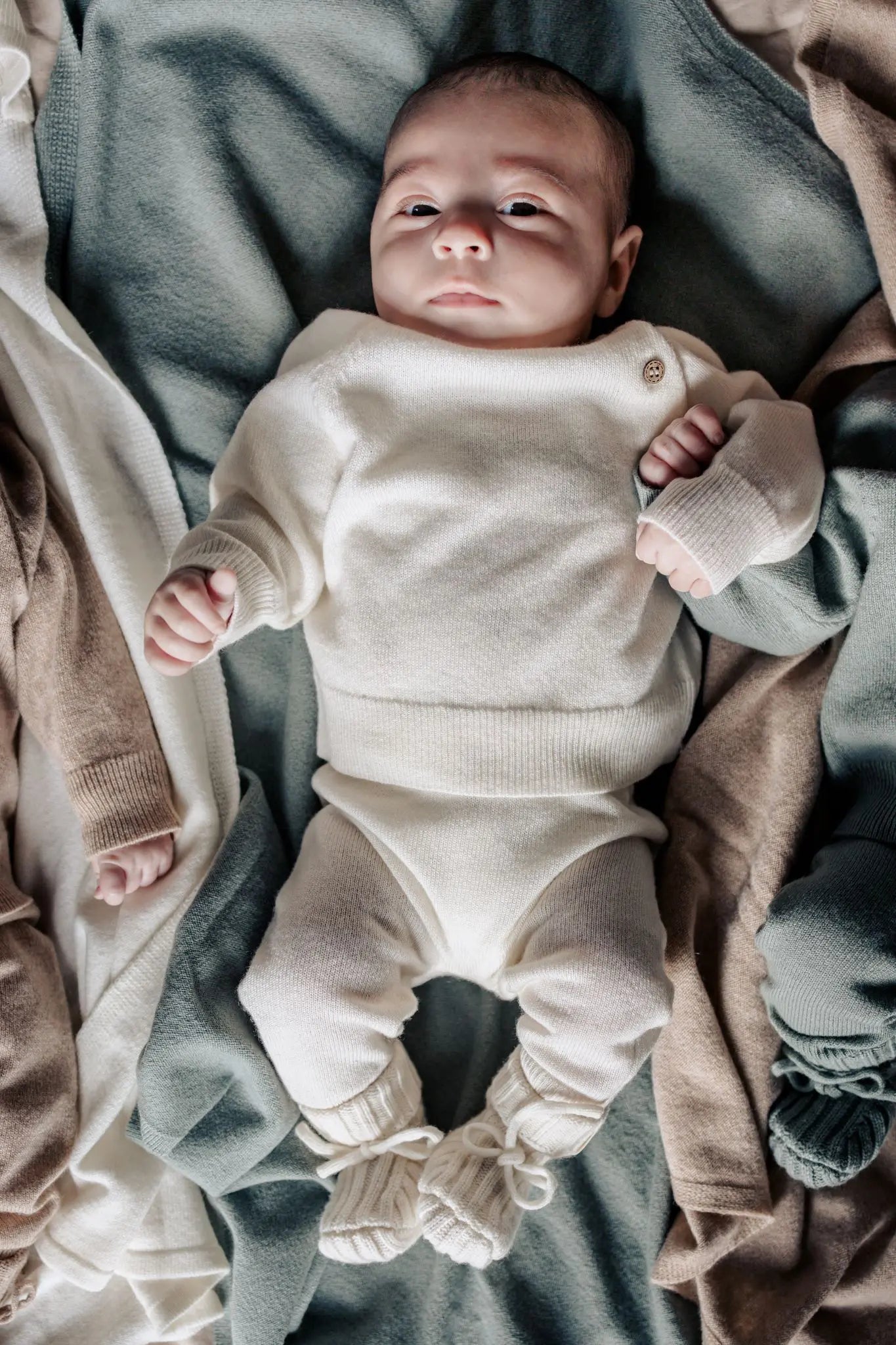 Baby in creme kleurige wollen setje bestaande uit broek, trui en slofjes