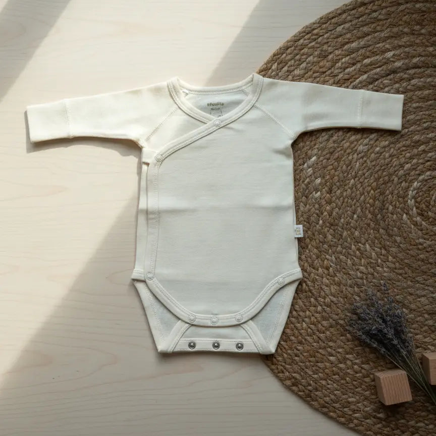 Ecru kleurige meegroei romper van merinowol en bamboe op een houten vloer en rieten kleed.