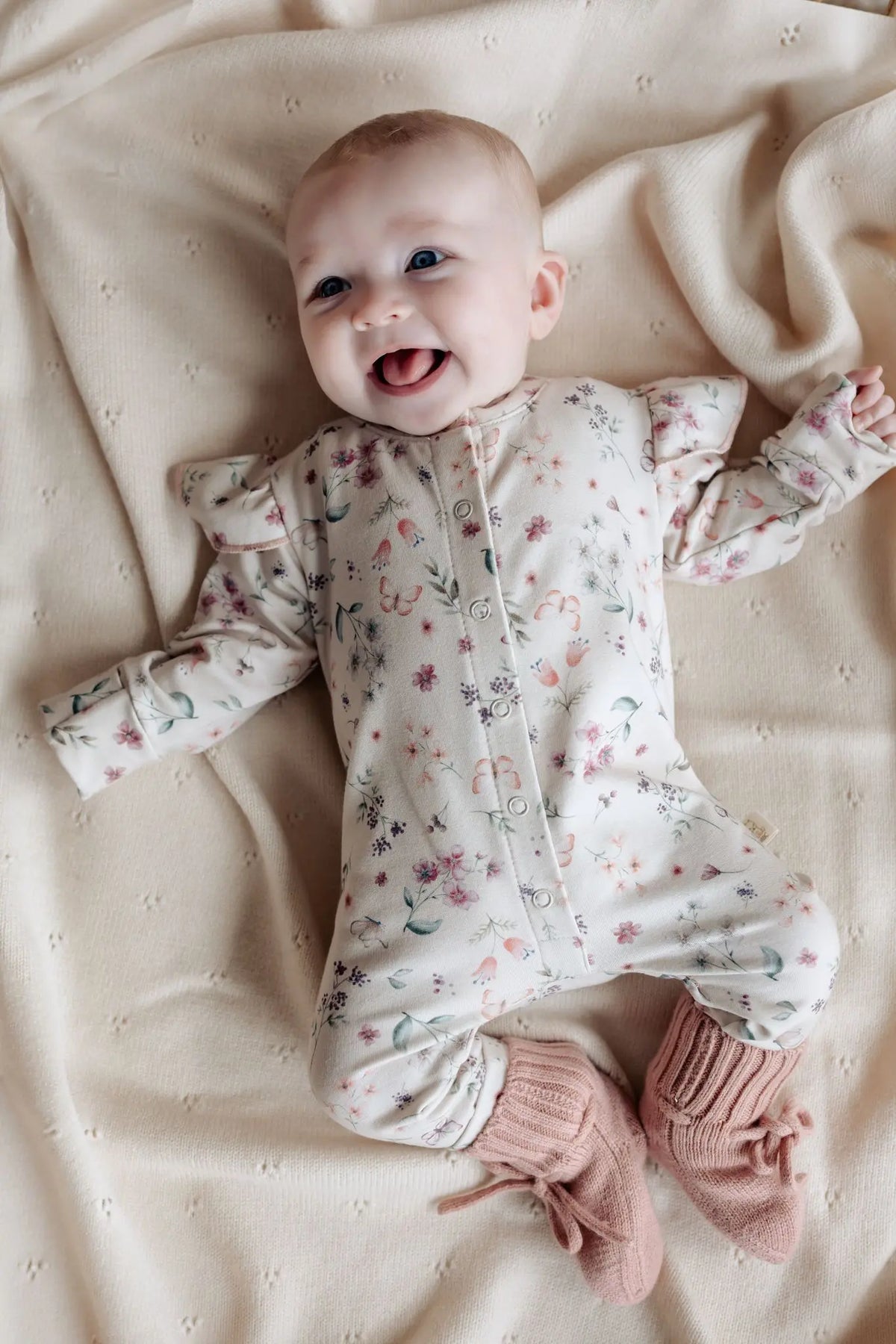 Lachende baby in zachtroze boxpakje met bloemen en vlinder print van Moalie