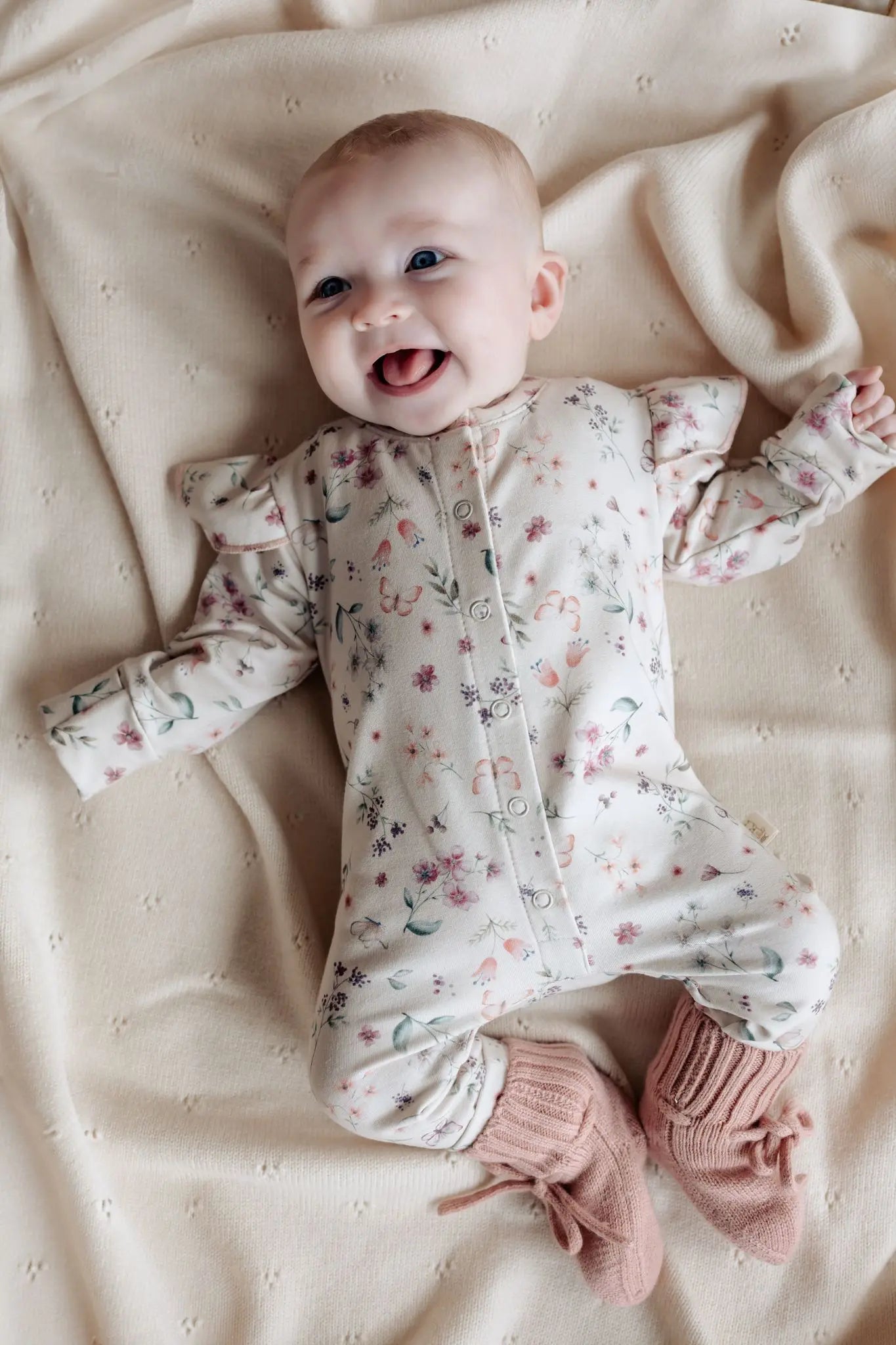 Lachende baby in zachtroze boxpakje met bloemen en vlinder print van Moalie