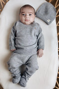 Bild in Galerie-Betrachter laden, Baby in grijs  pakje van merinowol en cashmere. De baby draagt een trui, broekje en slofjes in een zacht grijs gemeleerde tint. 
