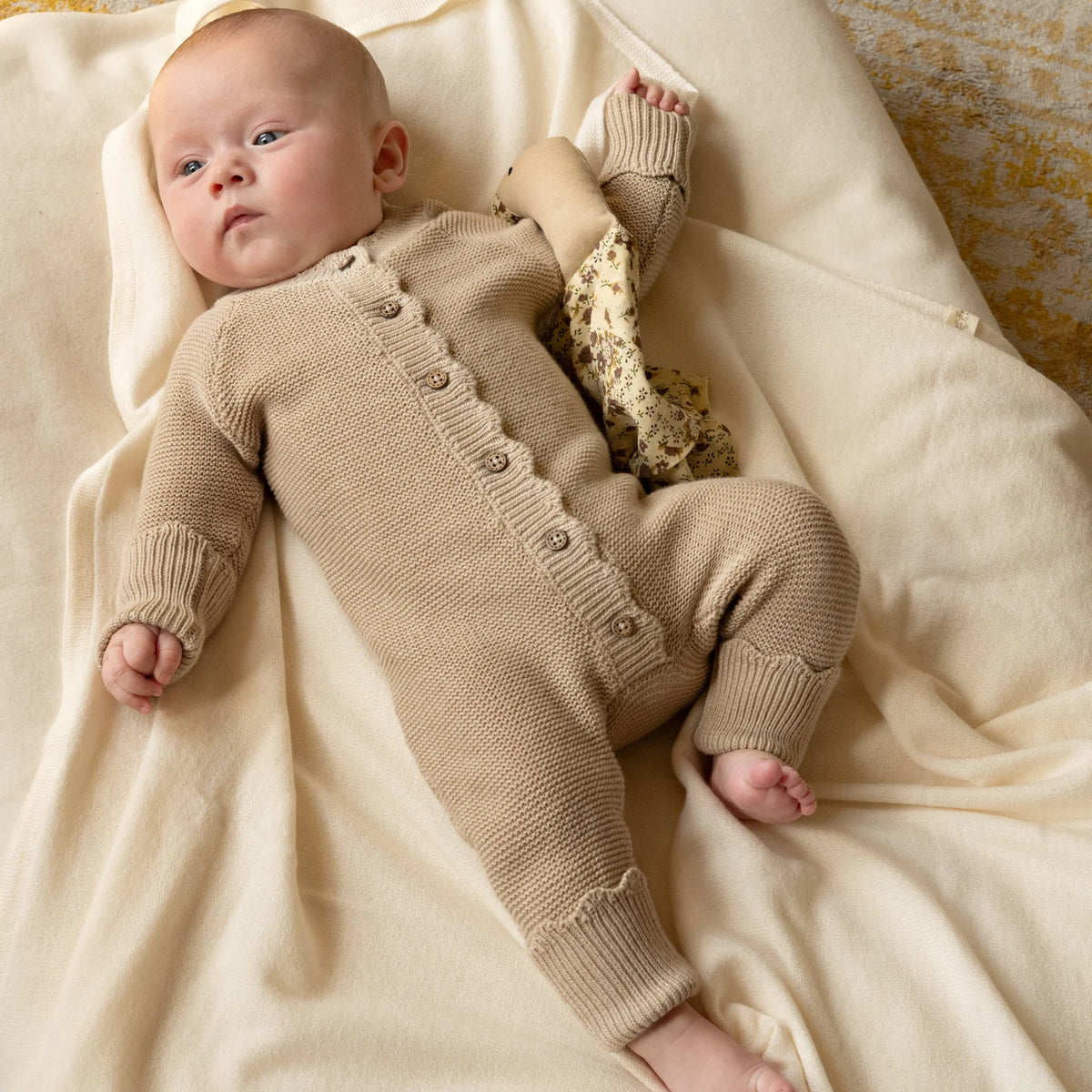 Baby liggend op cremekleurige deken in een beige gebreid boxpakje van zachte katoen