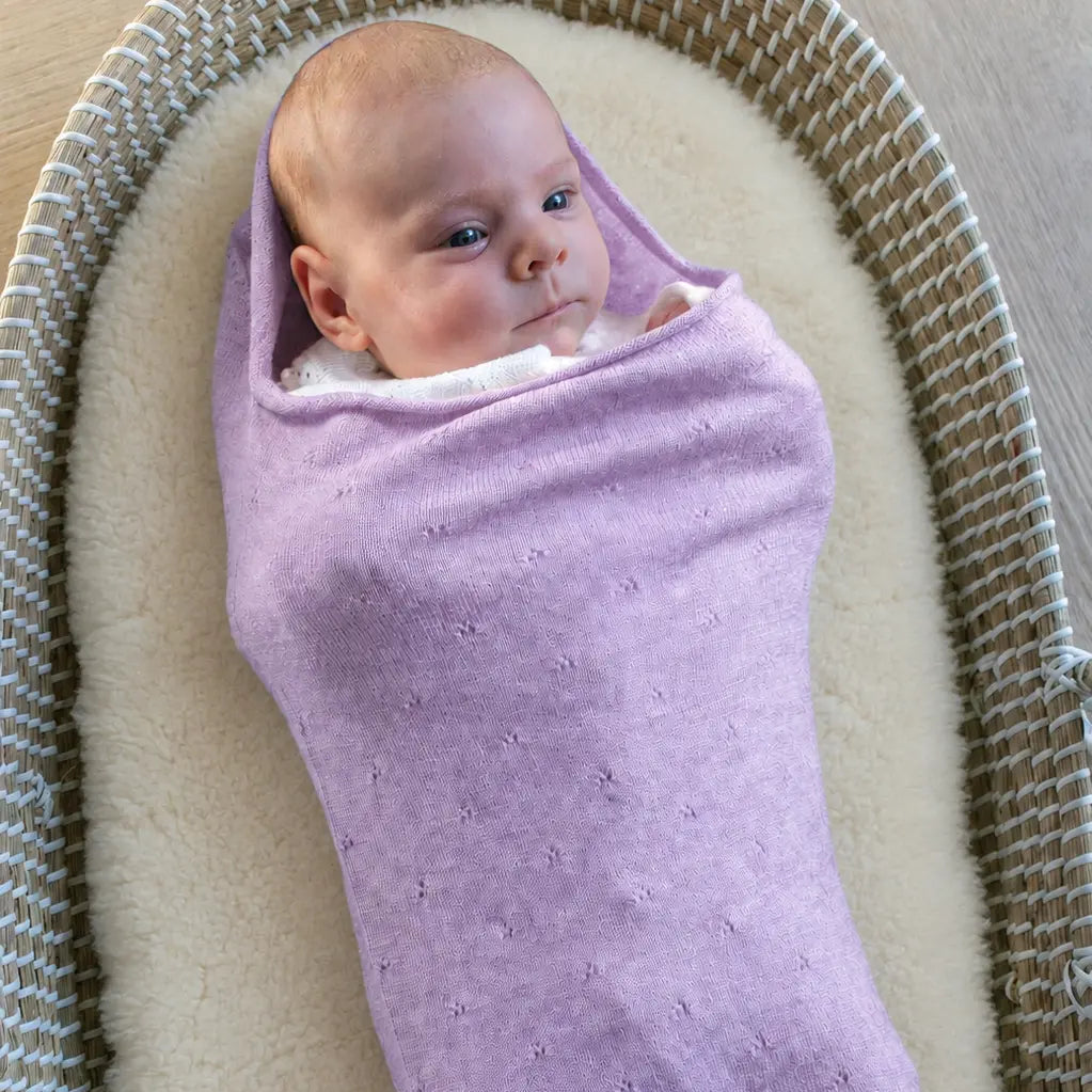 Baby in de Pointelle Snuggle Coco Lavender, een lila cocon van merinowol, in een rieten mandje
