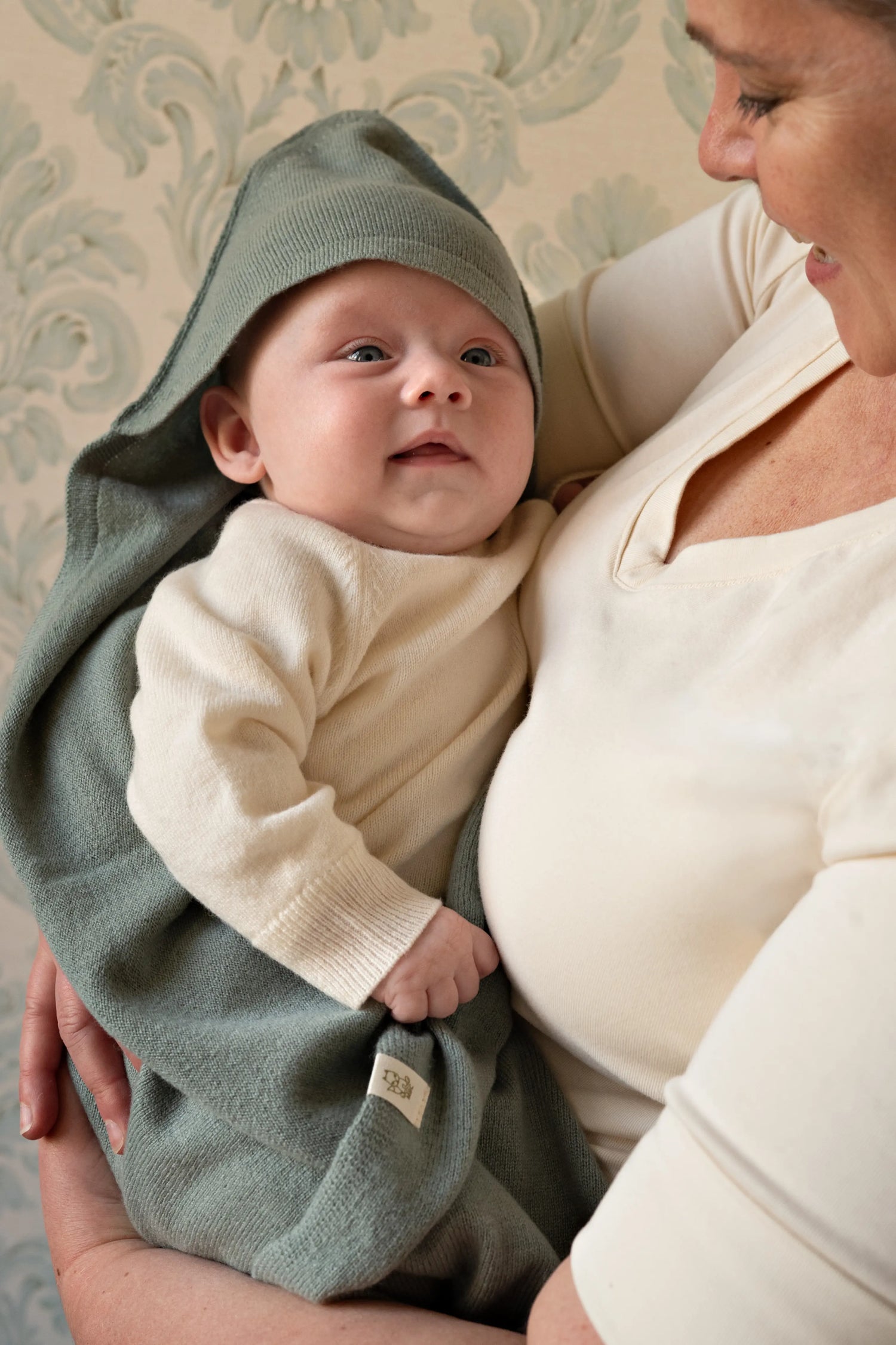 moeder met baby op dearm. De baby is gewikkeld in een sage groene omslagdoek van merinowol