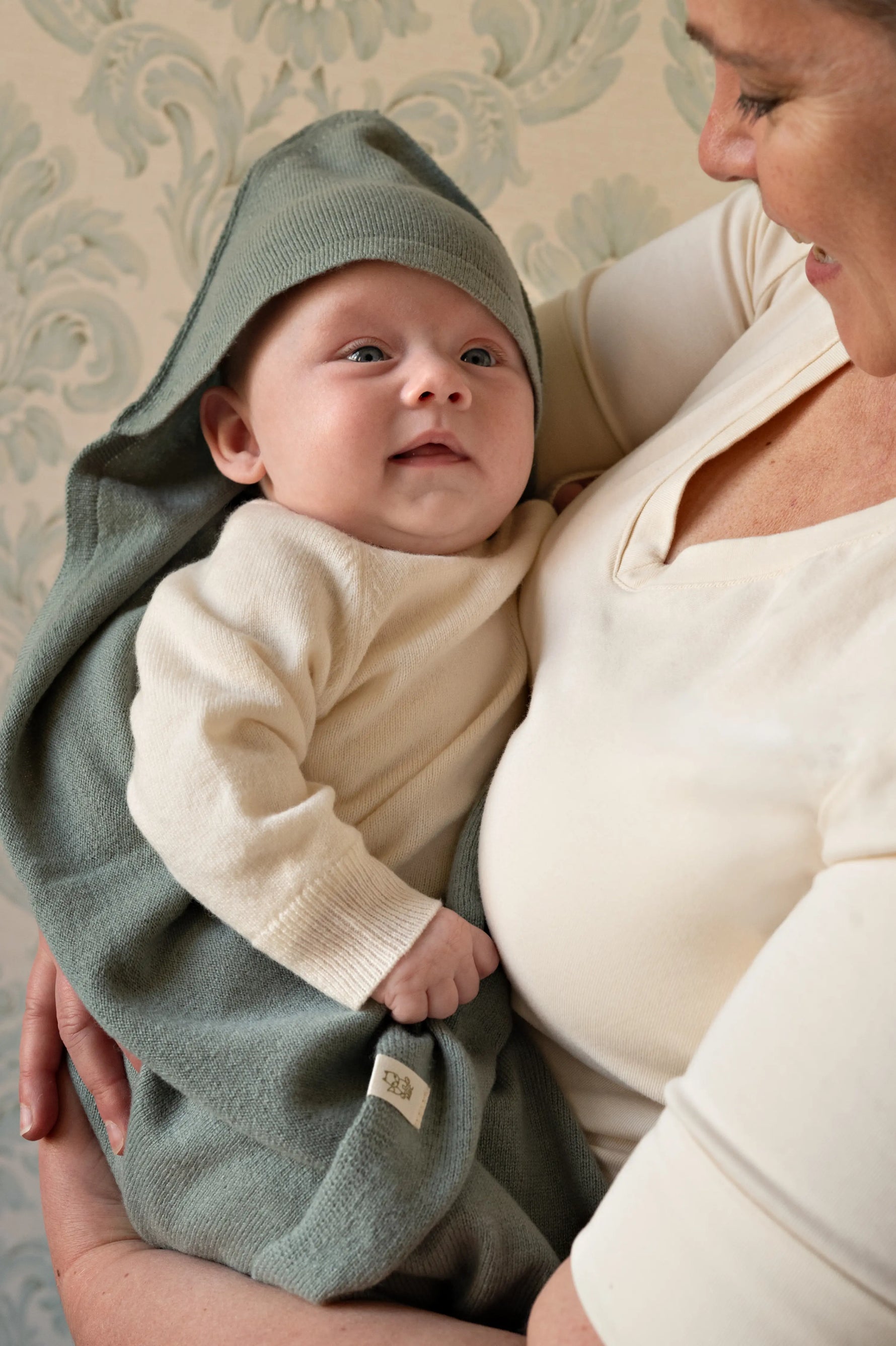 moeder met baby op dearm. De baby is gewikkeld in een sage groene omslagdoek van merinowol