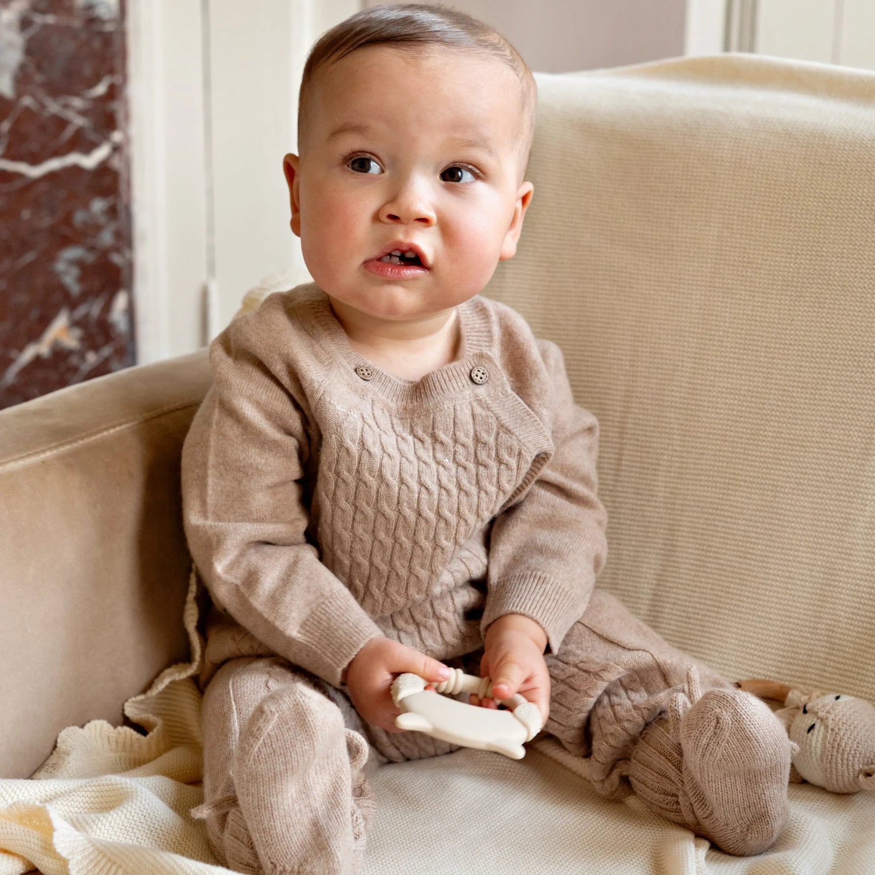 baby sitting in chair wearing a beige merinowool and cashmere babygrow