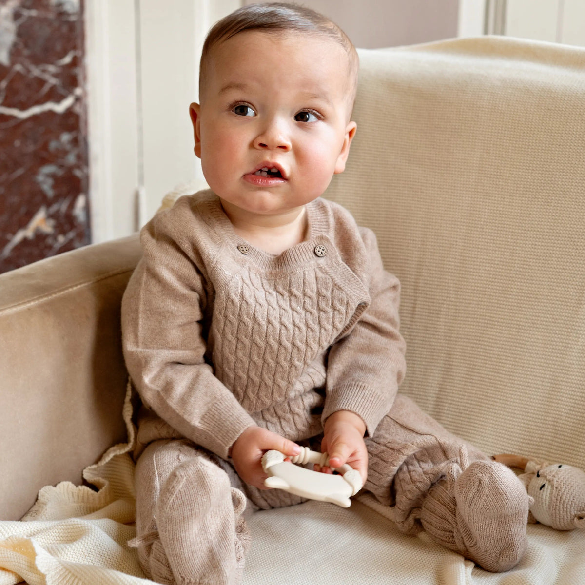 baby sitting in chair wearing a beige merinowool and cashmere babygrow