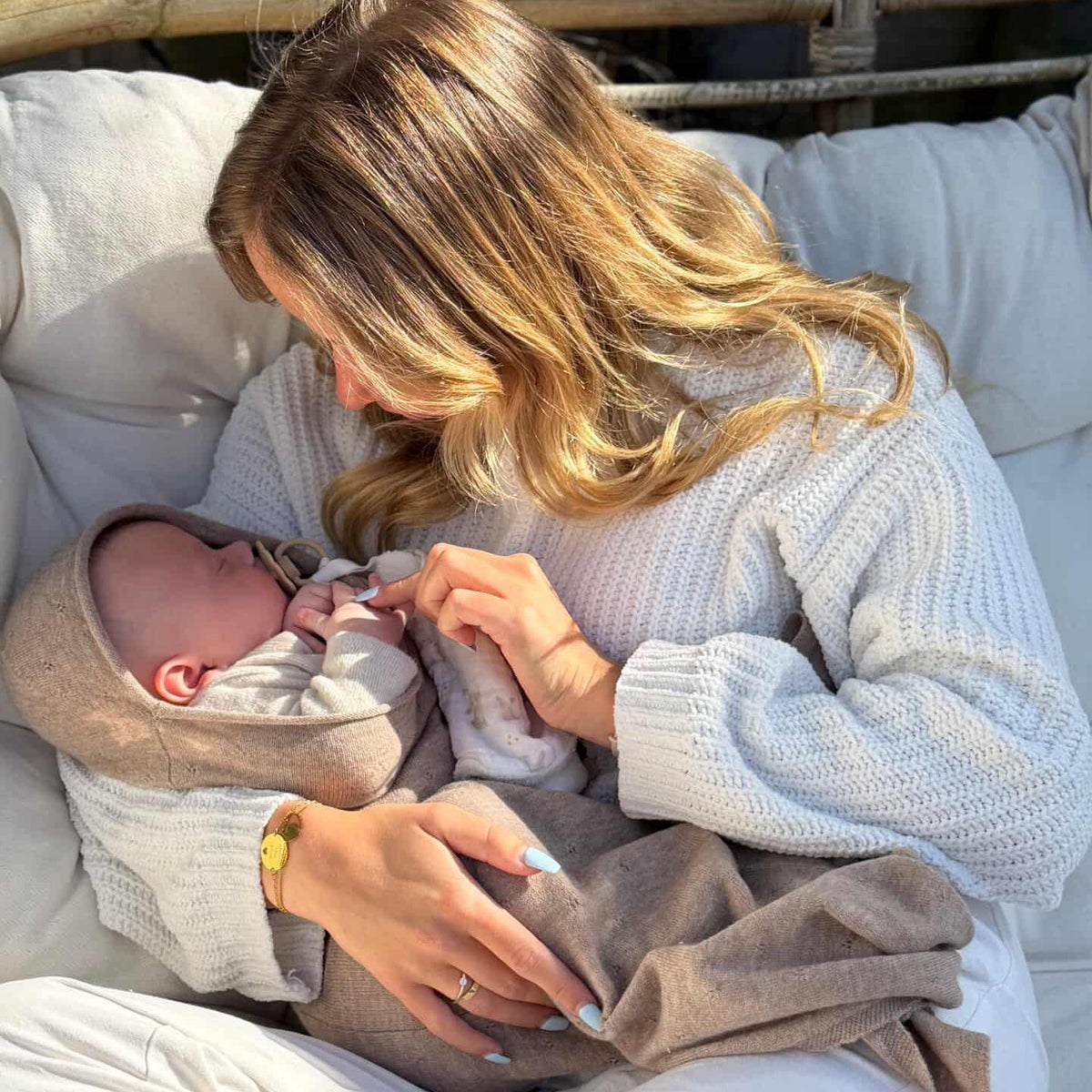 Mom and baby sitting outside in the sun. De baby is sleeping comfortably ia merinowool baby cocon in soft braun camel color. 