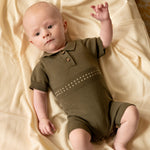 baby liggend om wllen creme kleurige deken. baby draagt een katoenen olijf groen gebreid zomerpakje voor baby's 