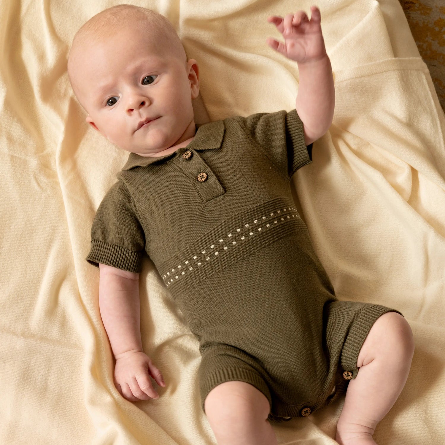 baby liggend om wllen creme kleurige deken. baby draagt een katoenen olijf groen gebreid zomerpakje voor baby's 