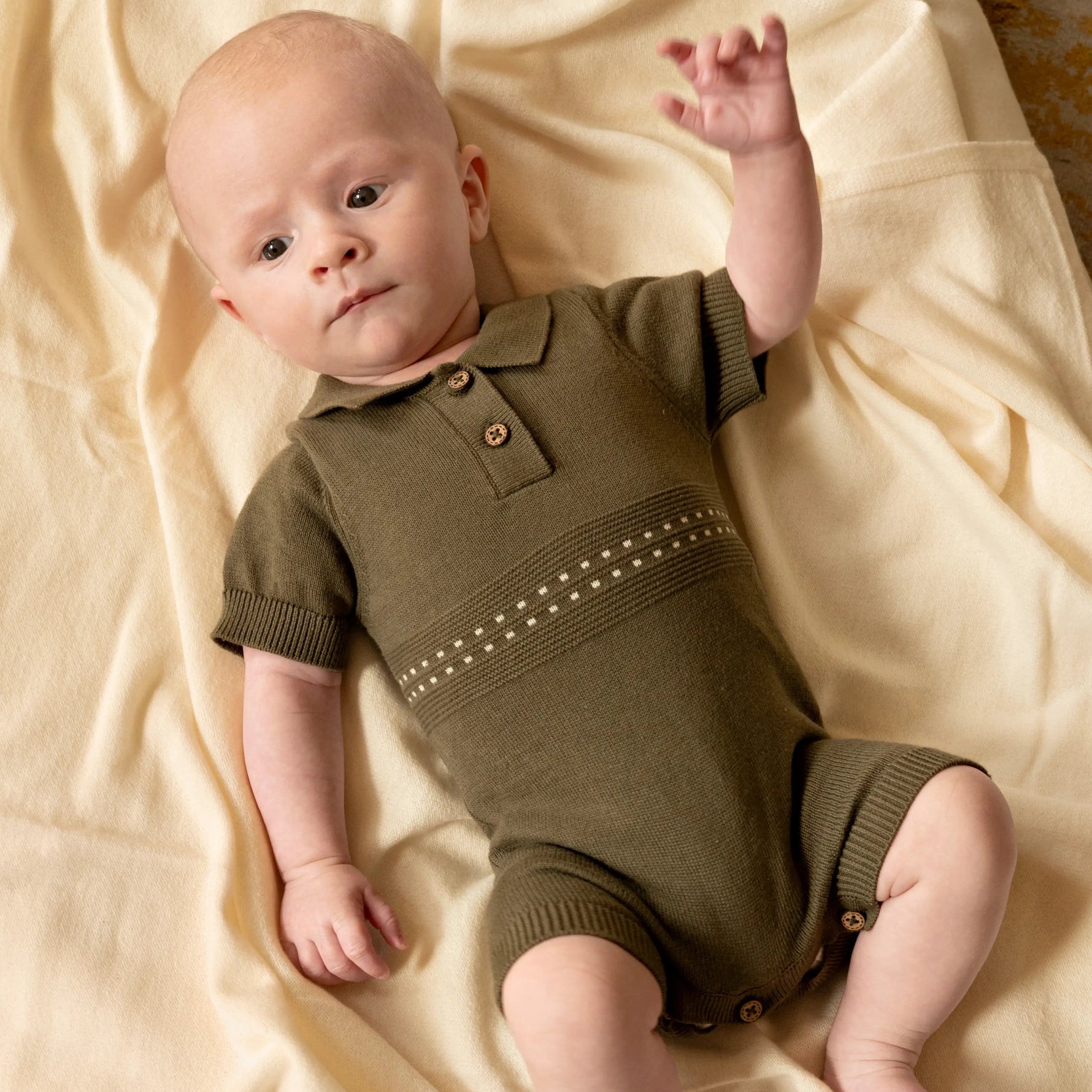 baby liggend om wllen creme kleurige deken. baby draagt een katoenen olijf groen gebreid zomerpakje voor baby's 