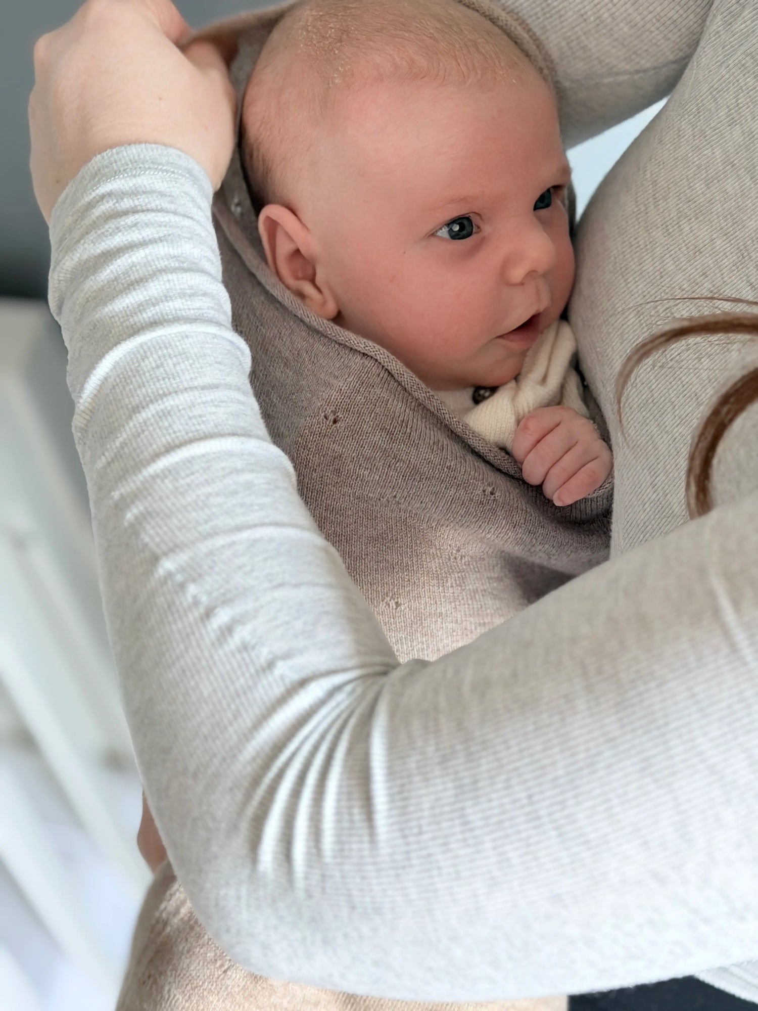 baby bij mdoer op schoot. Geborgen de babycocoon van Molie van pointelle gebreid merinowol en camelkleur.