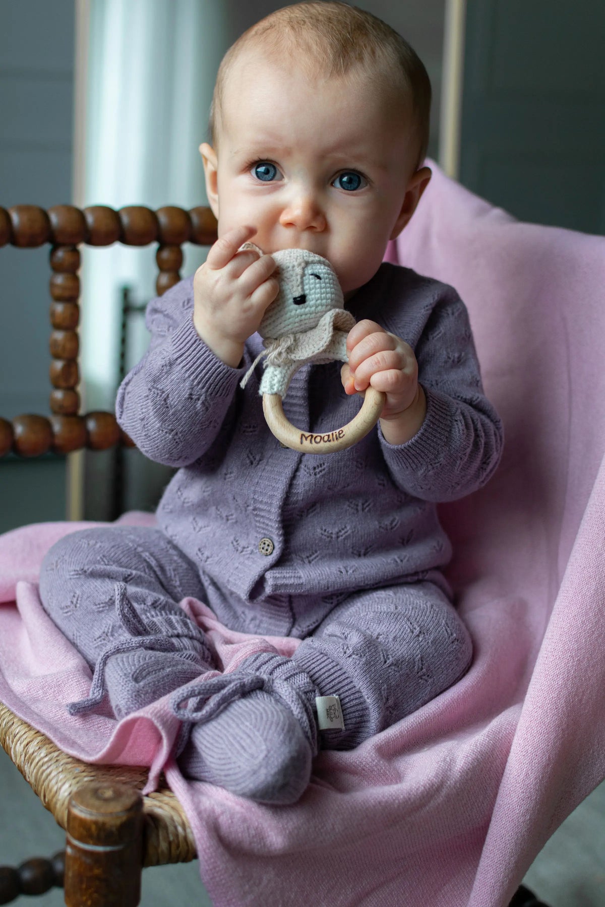 Baby zittend op roze merinowollen deken . De baby draagt een paarse outft van merinowol en cashmere
