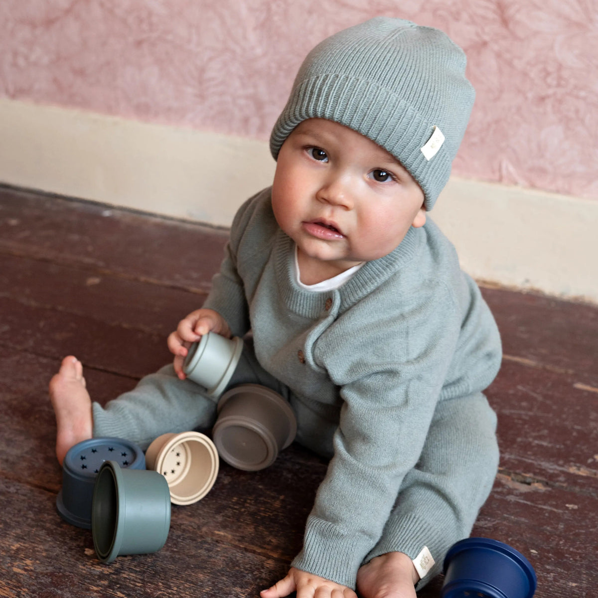 baby zittend op de grond in een sage groene merinowollen outfit van Moalie bestaande uit een mutsje, sweater en broekje