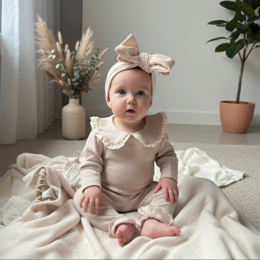 meisje van 7 maanden met haarband met grote strik in een kamer met beige en naturel kleuren. 