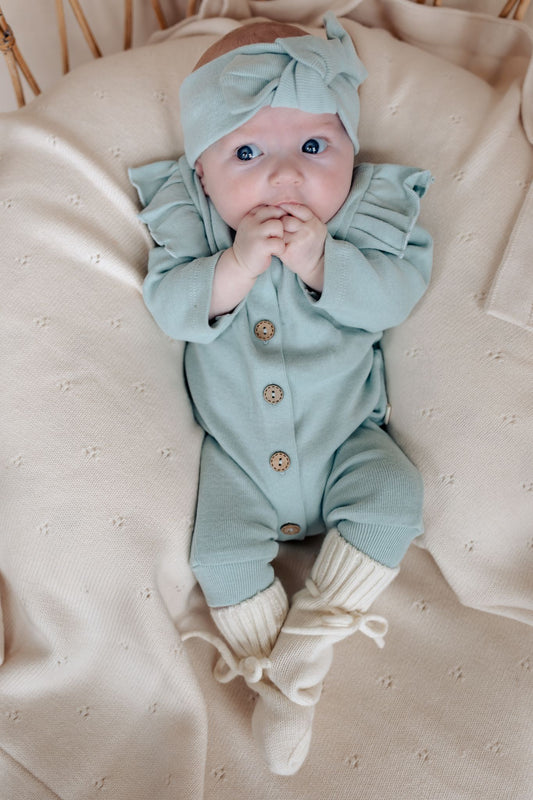 baby draagt turquoise boxpakje met ruffles en haarband op beige dekentje