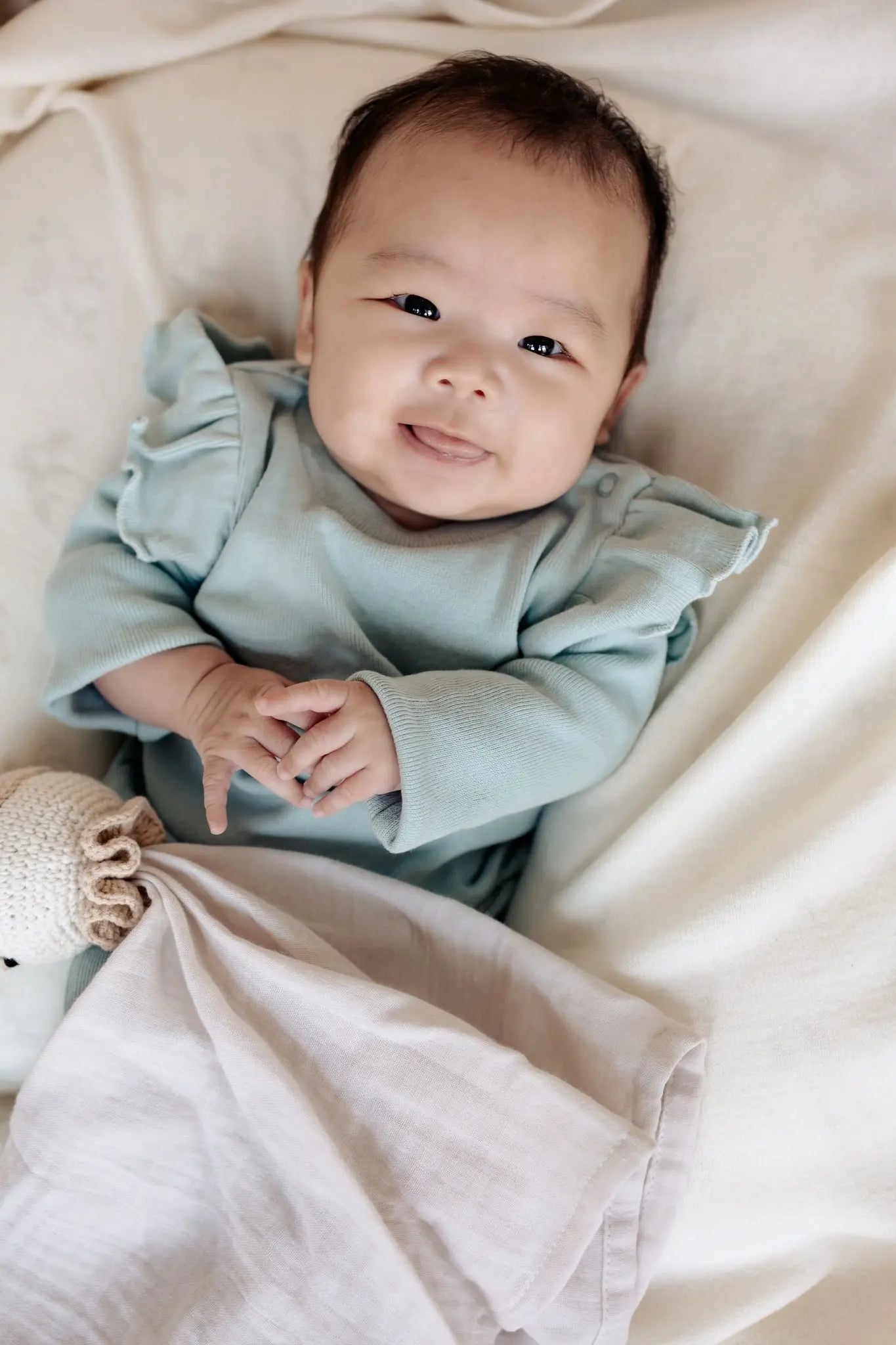 Lächelndes Baby in mintgrünem Pullover mit Rüschen 