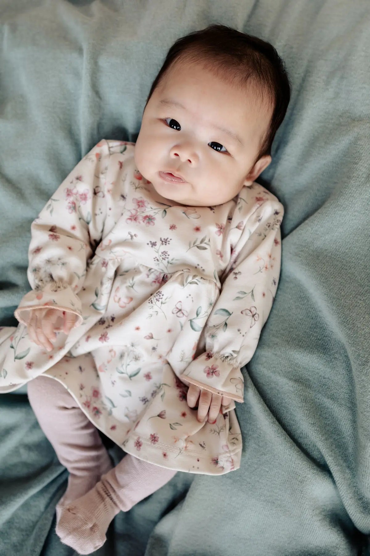 baby op een wollen sage groene deken die een Moalie jukrje draagt in zacht orze met bloemen en vlinder print 