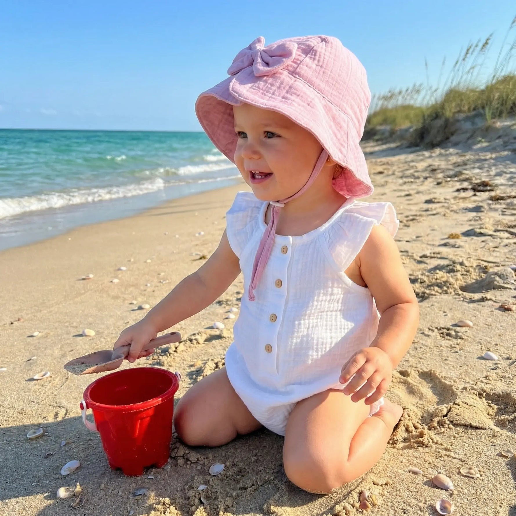 baby op strand met zonnehoedje van roze katoen