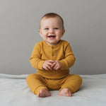 zittende lachende baby in okergeel bokpakje van biologisch ribkatoen 