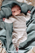 baby op sage groene wollen deken. de baby draagt een beige pakje van wafel katoen. 