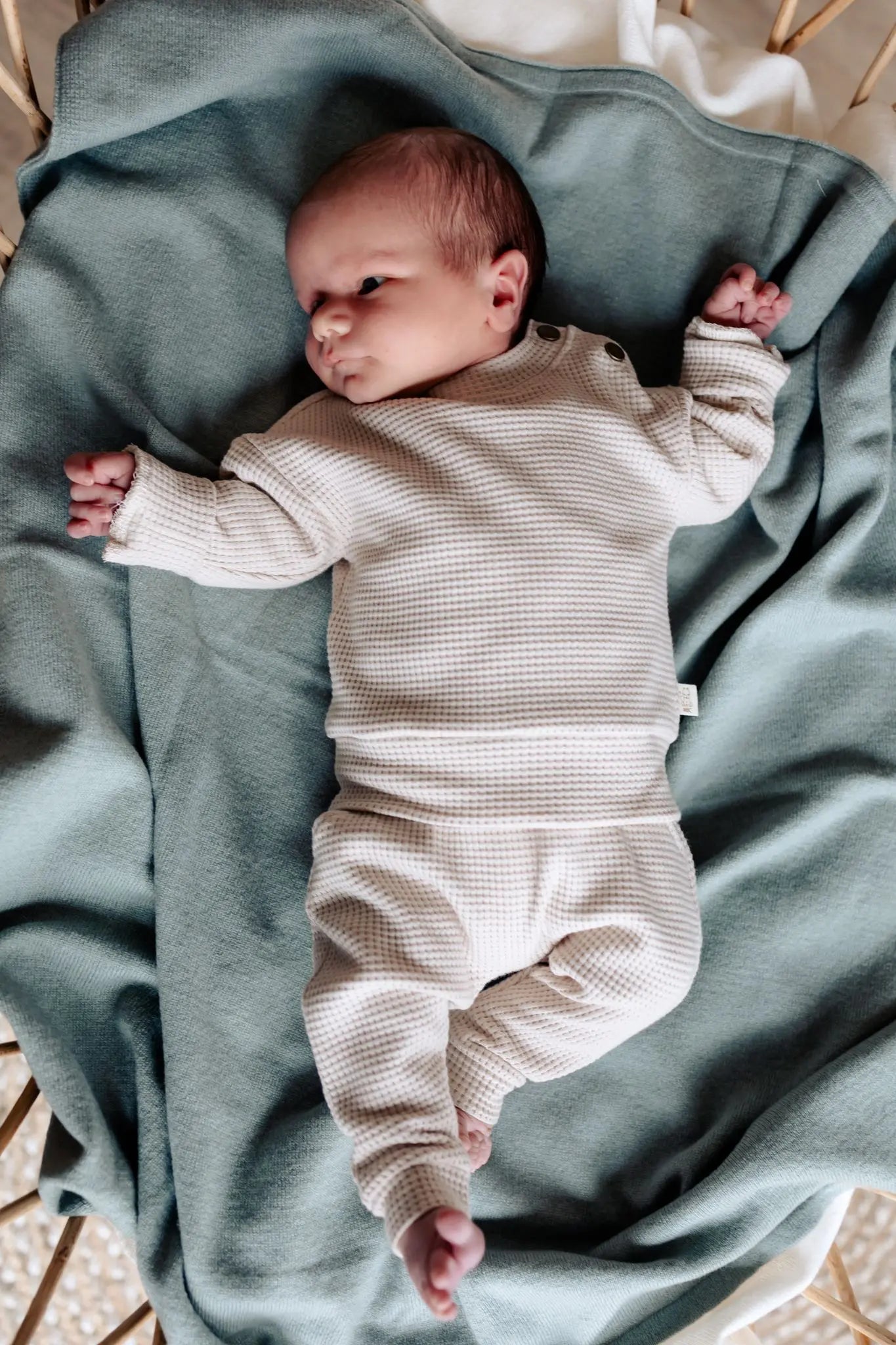 baby op sage groene wollen deken. de baby draagt een beige pakje van wafel katoen. 