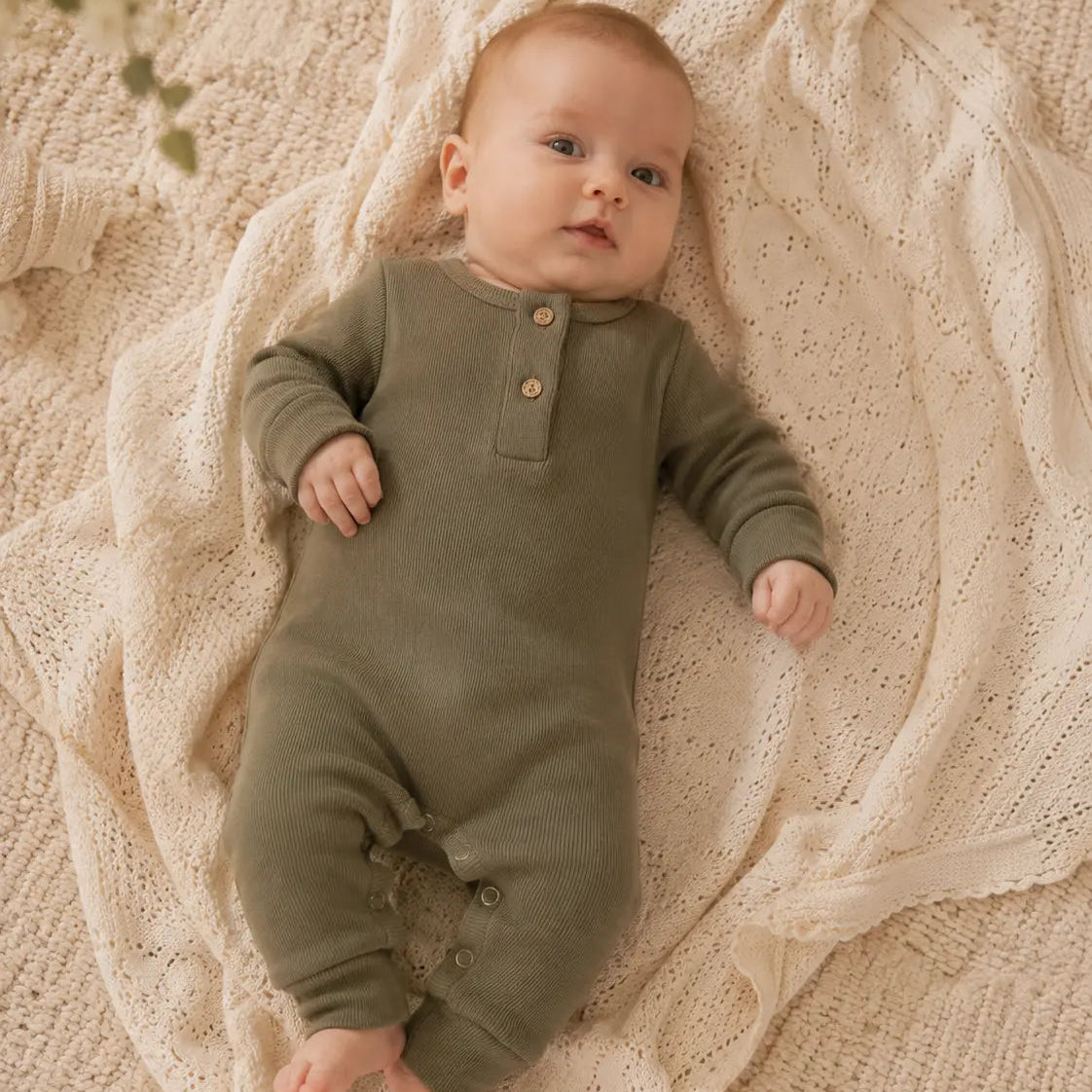 baby in donker groen katoenen boxpakje liggend op gehaakt kleed