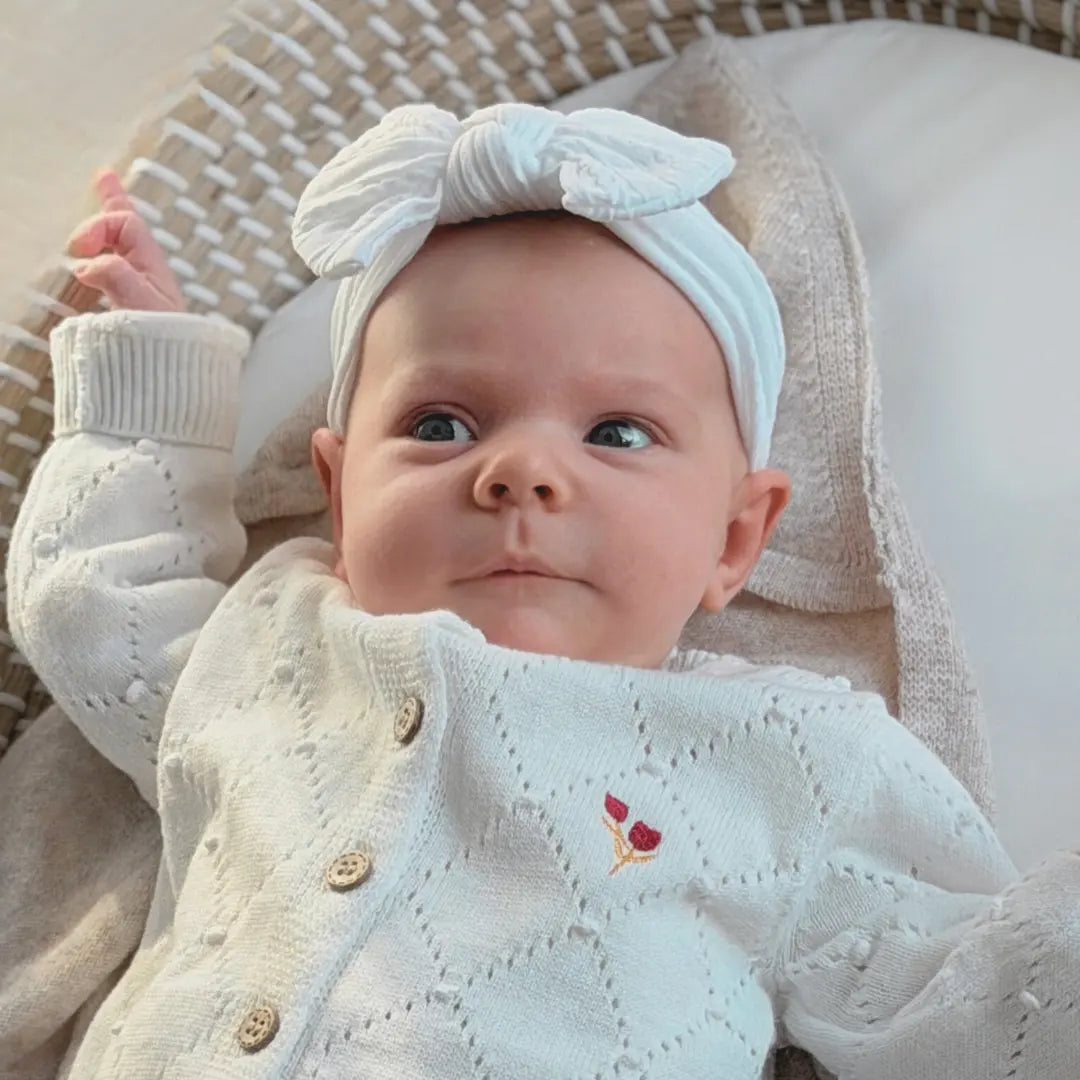 baby draagt wit gebreid katoenen veste met geborduurde tulpjes en een baby haarband in wit met strik