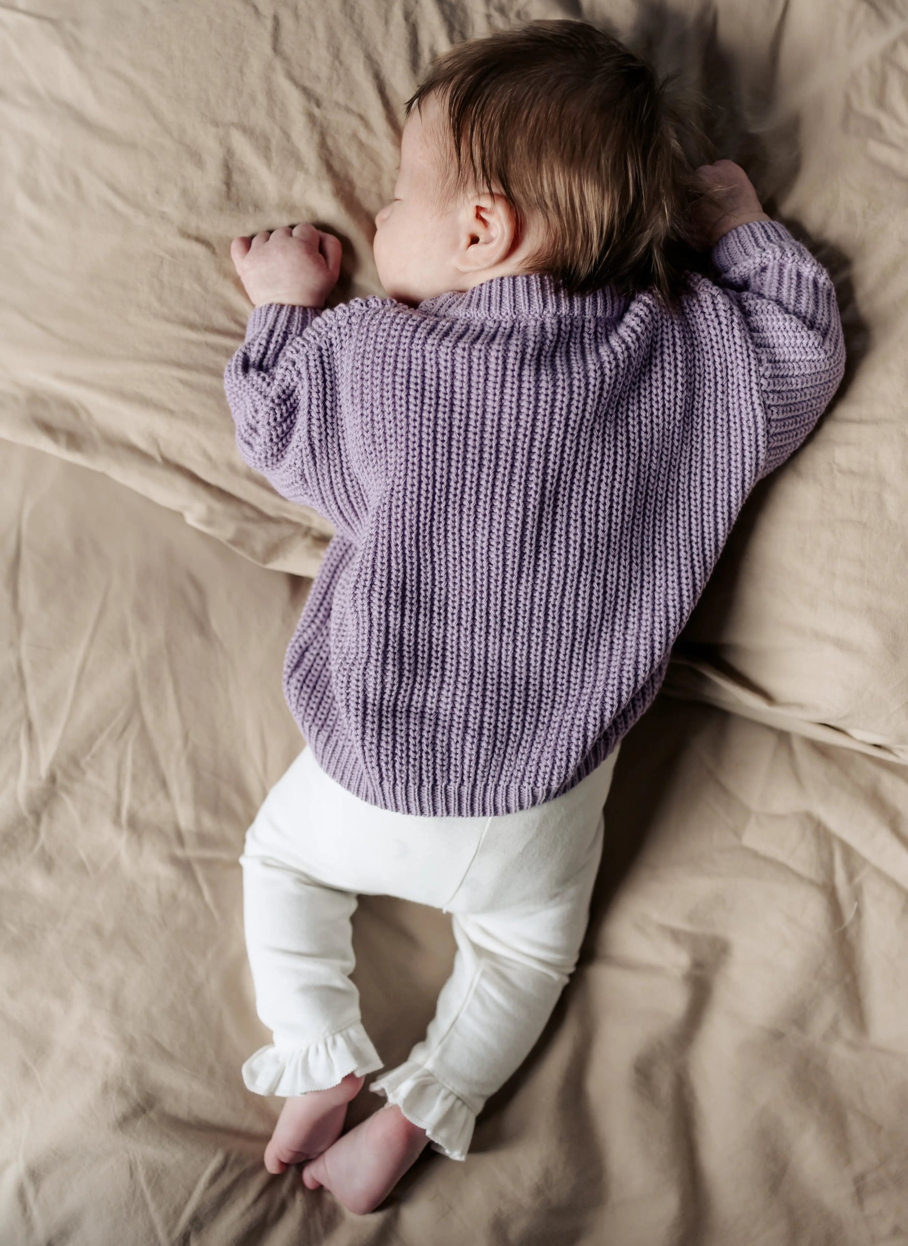 baby liggend op buik in lavender sweater en offwhite legging met ruches 