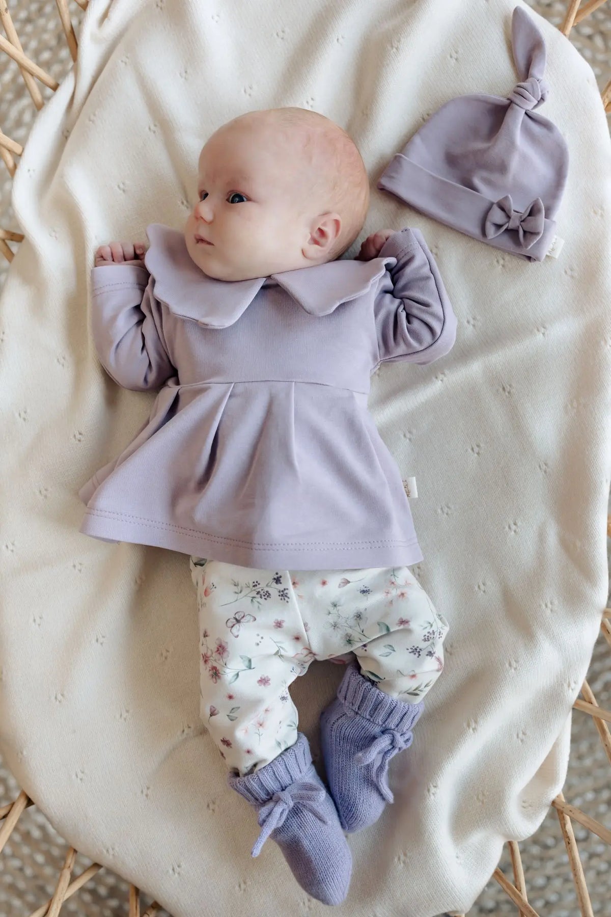 Baby in Moalie outfit: lila kleurig bloesje en slofjes en gebloemde broek