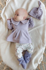Baby in Moalie outfit: lila kleurig bloesje en slofjes en gebloemde broek