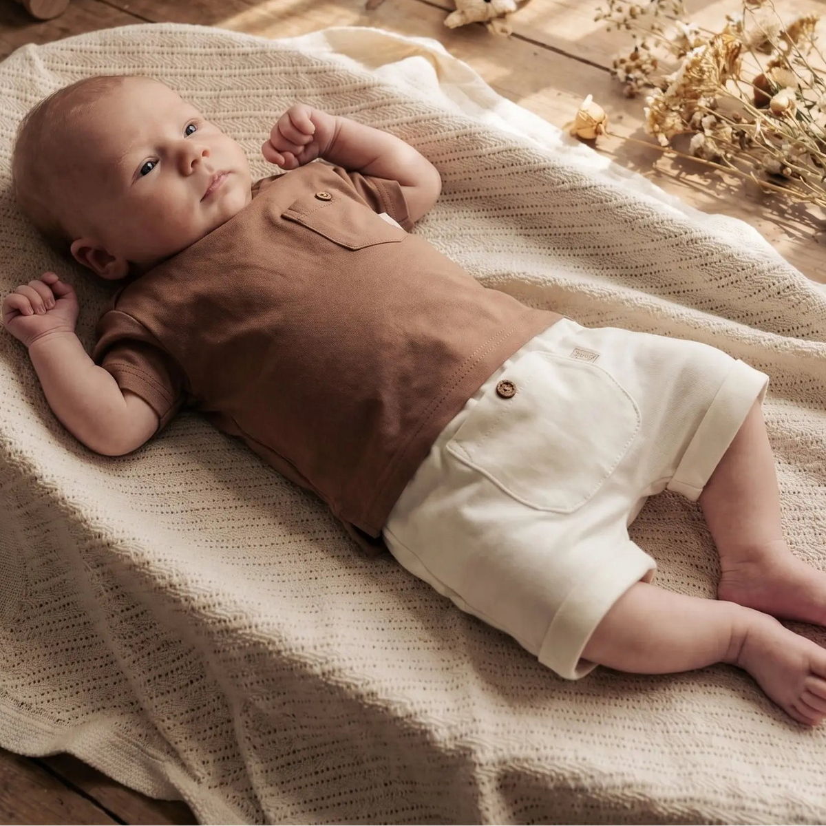 baby liggend in mandje op beige deken in off white baby short met knoopje en mokka bruin t-shirt 