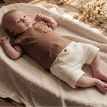 baby liggend in mandje op beige deken in off white baby short met knoopje en mokka bruin t-shirt 