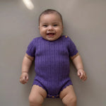 lachende baby in pointelle gebreide paarse romper 