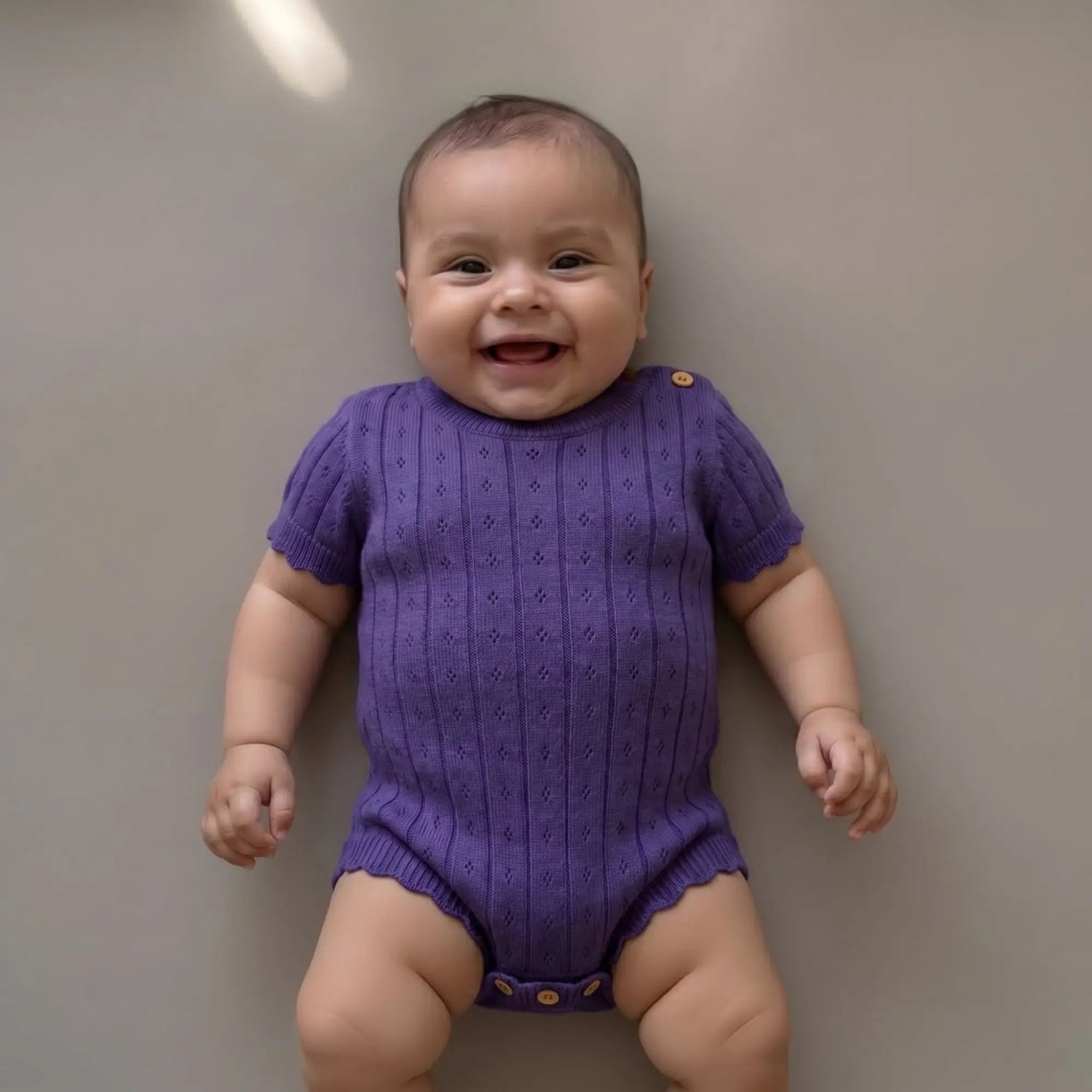 lachende baby in pointelle gebreide paarse romper 